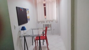 Una habitación pequeña y limpia con una mesa de vidrio y una silla roja, una lámpara azul y una pizarra con dibujos coloridos.