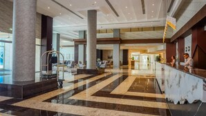 Eine geräumige Lobby mit Marmorboden, großen Säulen, einer Rezeption und Blick zu den Hotelzimmern.