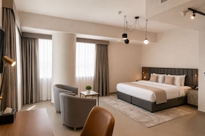 A modern hotel room with a large bed, two armchairs, a desk, and a small table with a plant.