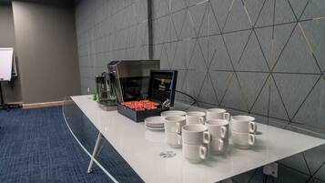 Une table de conférence avec une machine à café, des assiettes et des tasses.