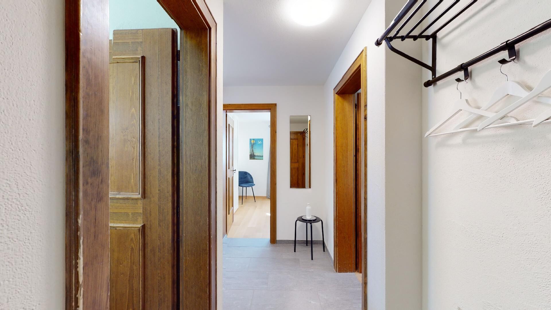 Ein Flur mit Holztüren, einem kleinen Hocker und einem an der Wand befestigten Wäscheständer.