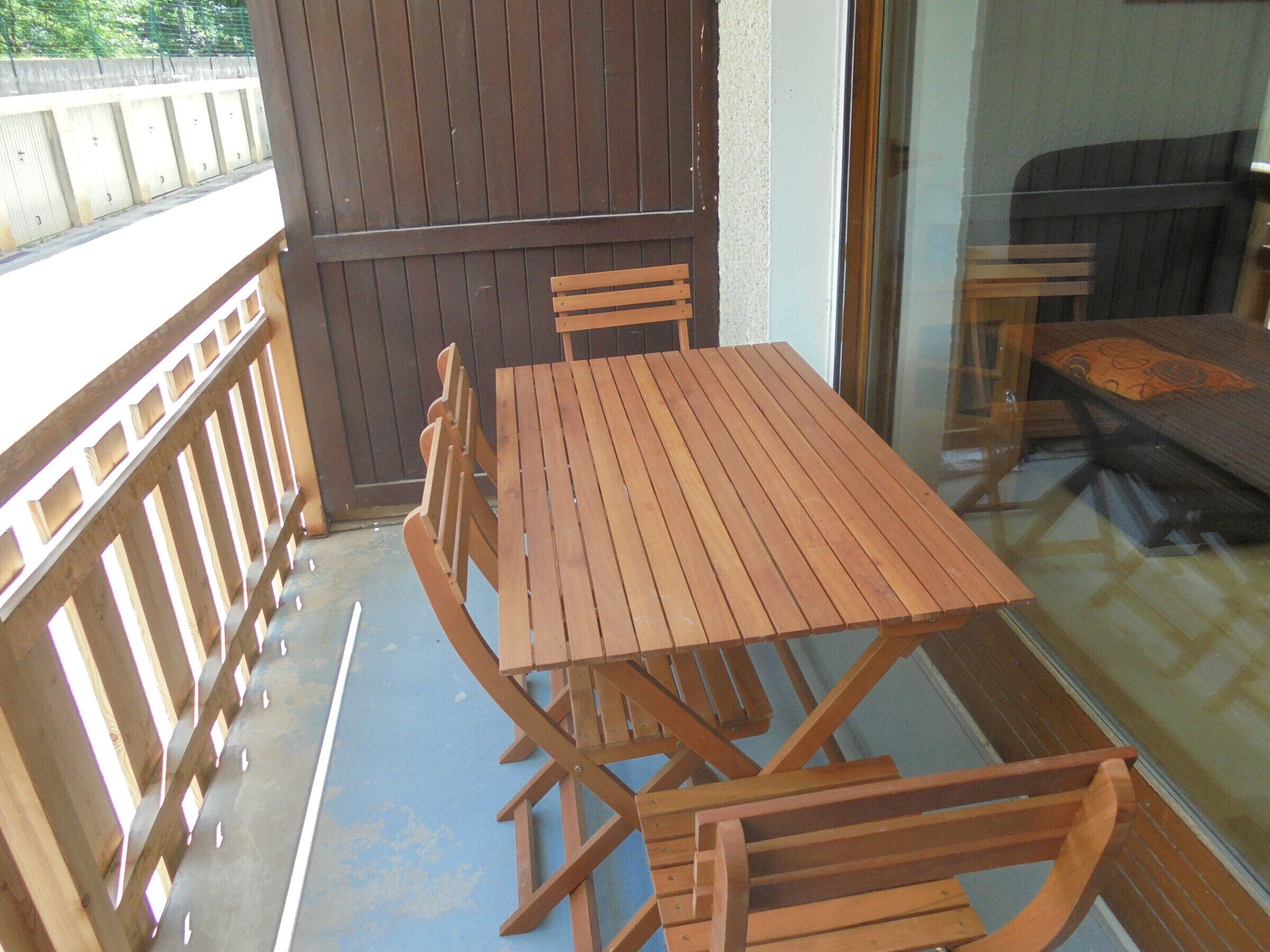A wooden table and chairs on a balcony with a view of a building.