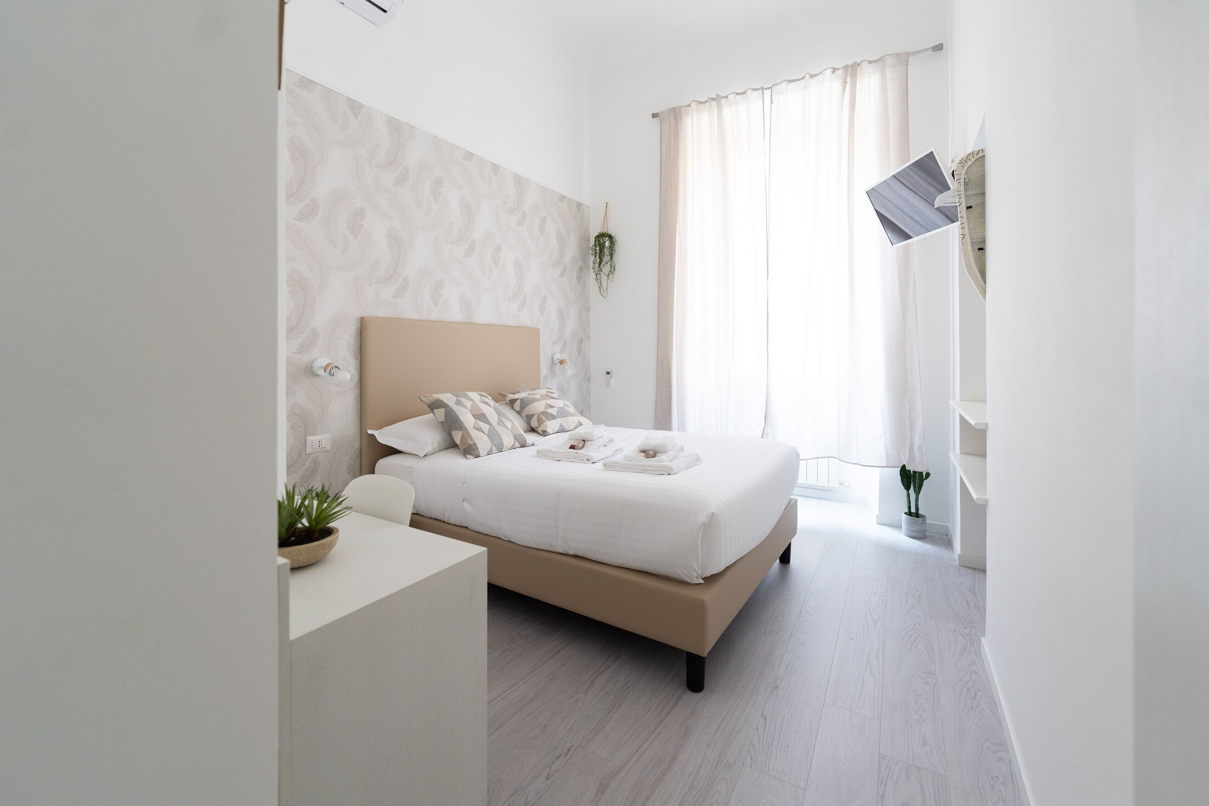 A modern bedroom with a large bed, a bedside table, a potted plant, and a window with curtains.