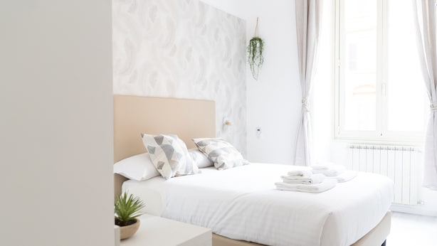 A modern bedroom with a large bed, a bedside table, a potted plant, and a view of the outdoors through a window. - White Gioberti Guesthouse (Rome)