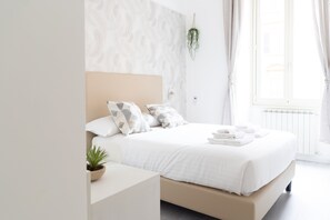 A modern bedroom with a large bed, a bedside table, a potted plant, and a view of the outdoors through a window. - White Gioberti Guesthouse (Rome)