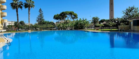 Una piscina azul cristalina rodeada de palmeras y una torre alta.