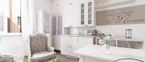 Una cocina moderna con armarios blancos, una zona de comedor con una mesa y sillas blancas, y un letrero decorativo en la pared.