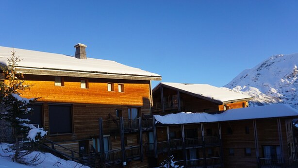 Un chalet en bois doté de plusieurs balcons, avec une montagne enneigée en arrière-plan.