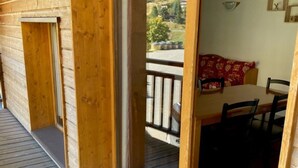 Une terrasse en bois avec une porte-fenêtre coulissante donnant sur un coin repas équipé d’une table et de chaises.