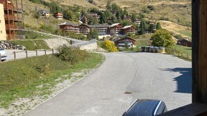 Une route de montagne menant à un ensemble de bâtiments en bois dotés de balcons, entourés de collines et de verdure.