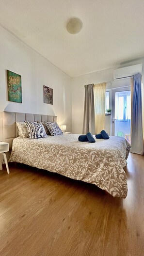 Une chambre à coucher comprenant un lit, une table de chevet, un climatiseur fixé au mur et une fenêtre avec des rideaux.