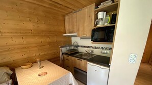 Ett kompakt kök med träväggar, ett litet matbord, en mikrovågsugn och en diskmaskin.