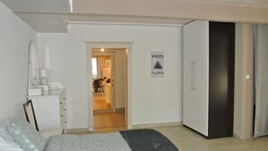 Un dormitorio con cama, armario, escritorio con lámpara y puerta que da a un baño.