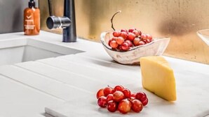A modern kitchen with a stainless steel sink, a bowl of red berries, and a wedge of cheese on the counter. - Stylish Chelsea Apartment on King’s Road (London)