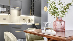 A modern kitchen with dark cabinetry, a wooden dining table, and a vase with green plants. - Stylish Chelsea Apartment on King’s Road (London)