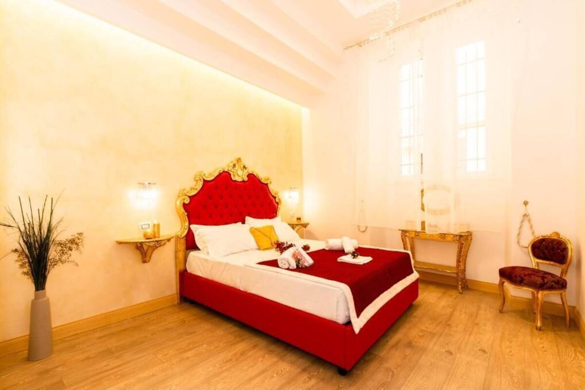 A room with a large bed, a bedside table, a chair, and a window.
