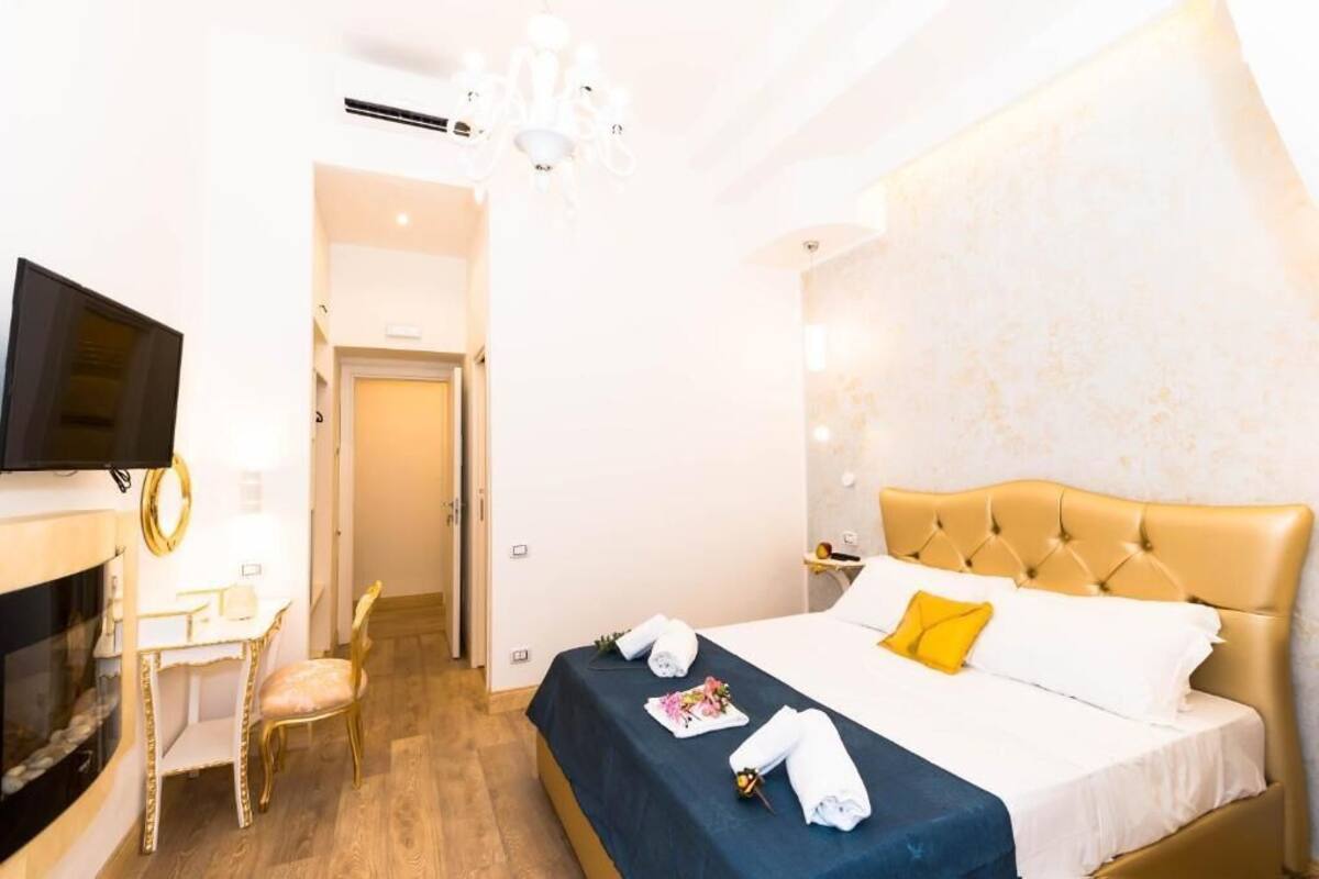 A hotel room with a bed, a desk, a chair, a television, and a chandelier.