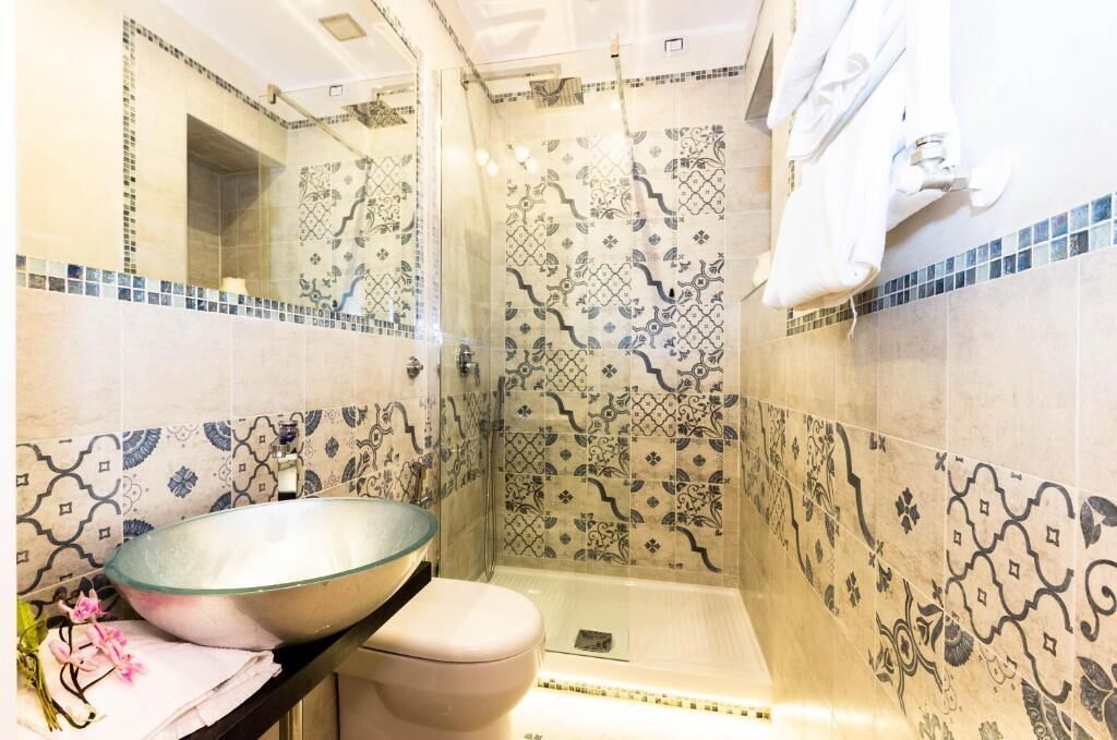 A bathroom with a glass bowl sink, a toilet, and a shower area with patterned tiles.