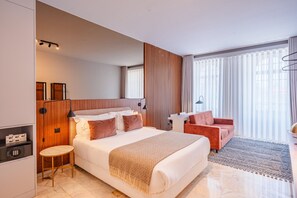 Ett modernt hotellrum med en stor säng, ett skrivbord, en stol och utsikt över staden genom stora fönster.