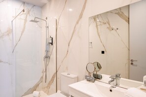 A modern bathroom with a glass-enclosed shower, a large mirror, and a white marble wall. - Retreat Studio in Bolhão Market (Oporto)