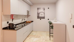 A modern kitchen with white cabinets, a black countertop, a microwave, and a coffee machine. There is a small bar area with a chair and a phone on the wall.