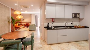 A modern kitchen with white cabinets, a microwave, and a dining area with a wooden table and green chairs.