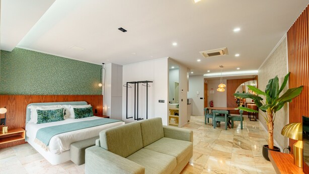 A hotel room with a bed, sofa, dining table, and a plant.