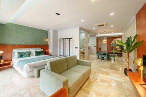 Una habitación de hotel con cama, sofá, zona de comedor y una planta.