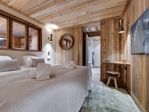 A bedroom with a large bed, wooden walls, a round mirror, a small stool, and a mounted picture.