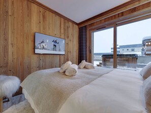 A wooden-paneled room with a large bed, a framed picture on the wall, and a view through a window.