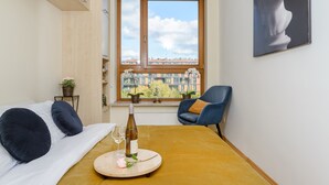 Une chambre à coucher avec un lit, une table sur laquelle se trouvent une bouteille et des verres, une chaise et une fenêtre donnant sur des immeubles.
