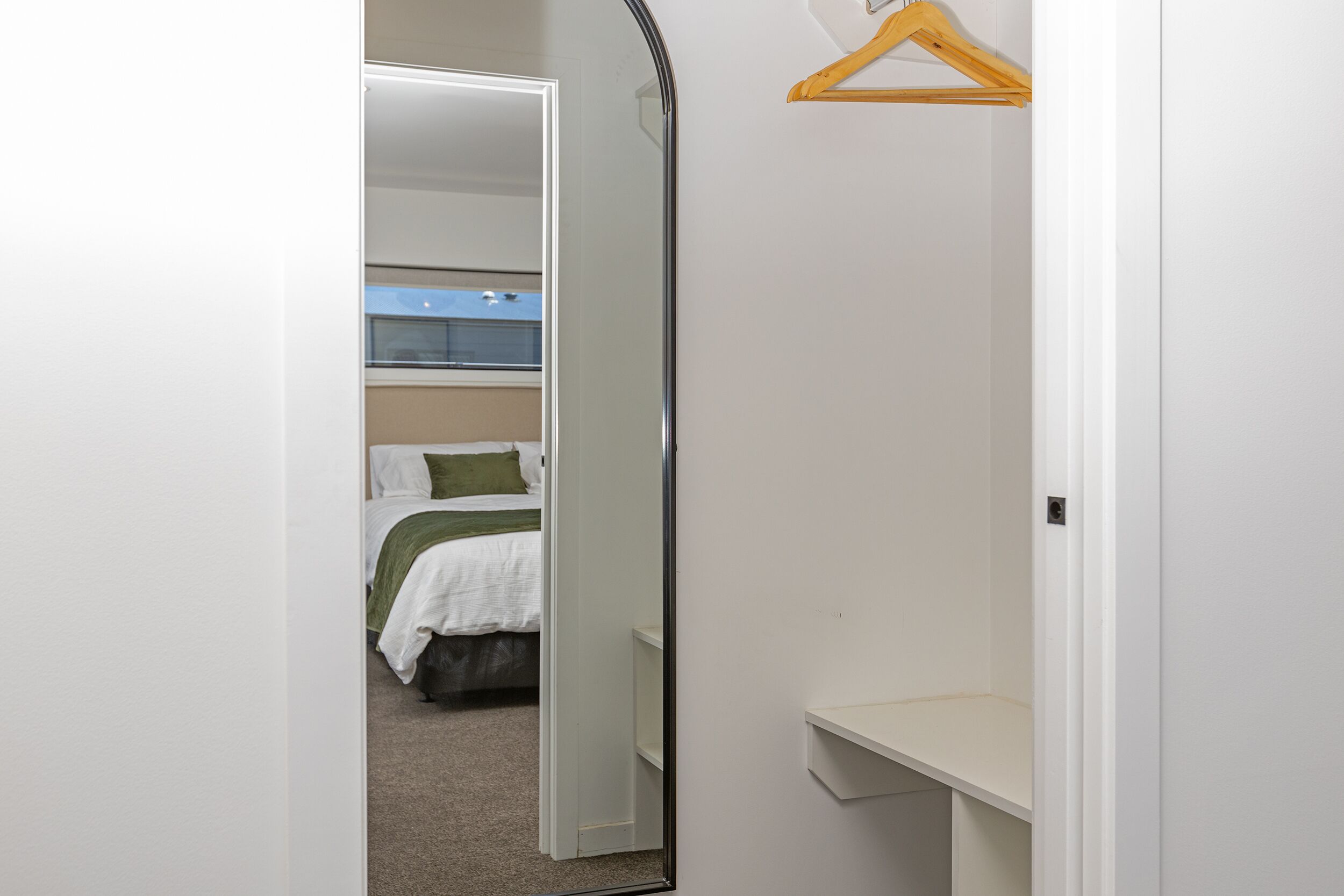 Ein Schlafzimmer mit einem Bett, einem Spiegel, einem hölzernen Kleiderbügel und einem weißen Regal.