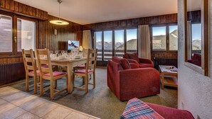 Un comedor con una mesa y sillas de madera, un sofá rojo y ventanas amplias con vista a las montañas.