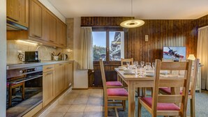 Una cocina con armarios de madera, una mesa de comedor para cuatro personas y vistas a un paisaje montañoso a través de una ventana.