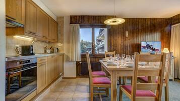 Une cuisine avec des meubles en bois, une table à manger dressée pour quatre personnes et une vue sur un paysage montagneux par la fenêtre.
