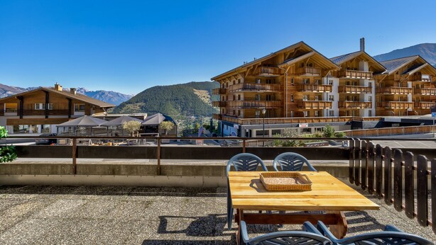 A wooden chalet-style building with multiple balconies, a gravel patio with a wooden table and chairs, and a mountain backdrop. - Appartement Savoleyres 30 - La Tzoumaz, 4 Vallees (La Tzoumaz)