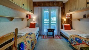 A room with two beds, wooden walls, a window with curtains, and a small table. - Appartement Savoleyres 30 - La Tzoumaz, 4 Vallees (La Tzoumaz)