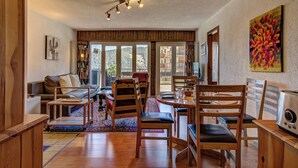 A spacious living area with a wooden floor, a dining table with chairs, a sofa, and a large window offering a view of the outdoors. - Appartement Savoleyres 30 - La Tzoumaz, 4 Vallees (La Tzoumaz)