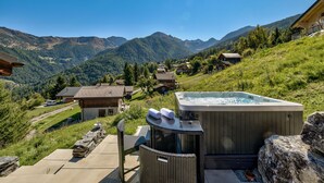 A hot tub on a patio with a mountain view, surrounded by houses and greenery. - Chalet Bellevue - Jacuzzi - Views - La Tzoumaz, 4 Vallees (La Tzoumaz)