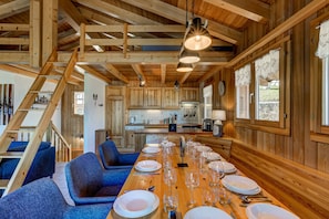 Un intérieur en bois avec une table à manger dressée pour le repas, des chaises rembourrées de tissu bleu et un escalier.