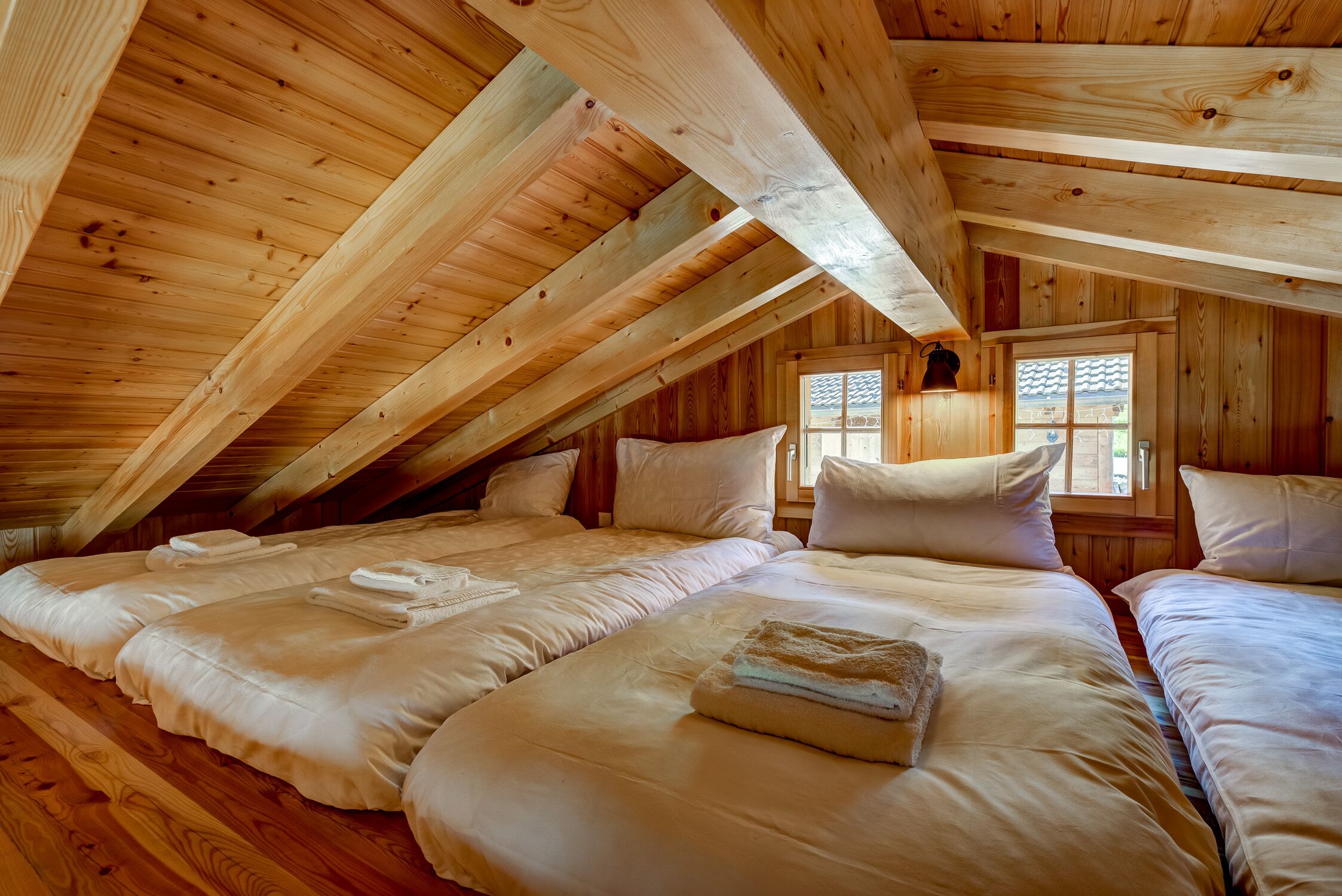 A cozy attic bedroom with wooden beams, two beds, and a window with a view.
