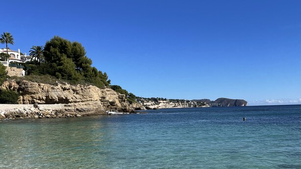A coastal scene with clear shallow waters, rocky cliffs, and a building with a white facade on the left. - Genuine Spanish villa - large private pool - close to the beach - sun all day (Benissa)