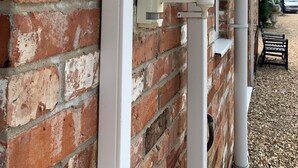 A brick wall with a white gutter and a white outdoor lamp.