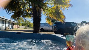 A pool area with a palm tree, a white building with a sign reading "1 M BATHROOMS", and a black vehicle parked nearby.