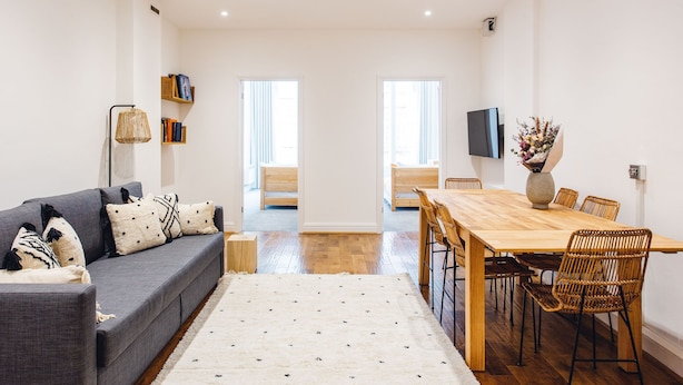 A modern living room with a grey sofa, a wooden dining table, wicker chairs, and a ceiling fan. - 2 Bed Apartment Right on Trafalgar Square  (London)
