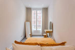 A hotel room with a bed, a wooden desk, a mirror, and a window with curtains.