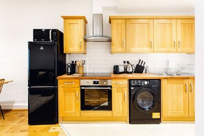 A compact kitchen with wooden cabinets, a black refrigerator, an oven, a dishwasher, and a sink.