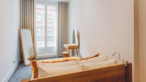 A bedroom with a wooden bed, a bedside table, a mirror, and a window with curtains. - 2 Bed Apartment Right on Trafalgar Square  (London)