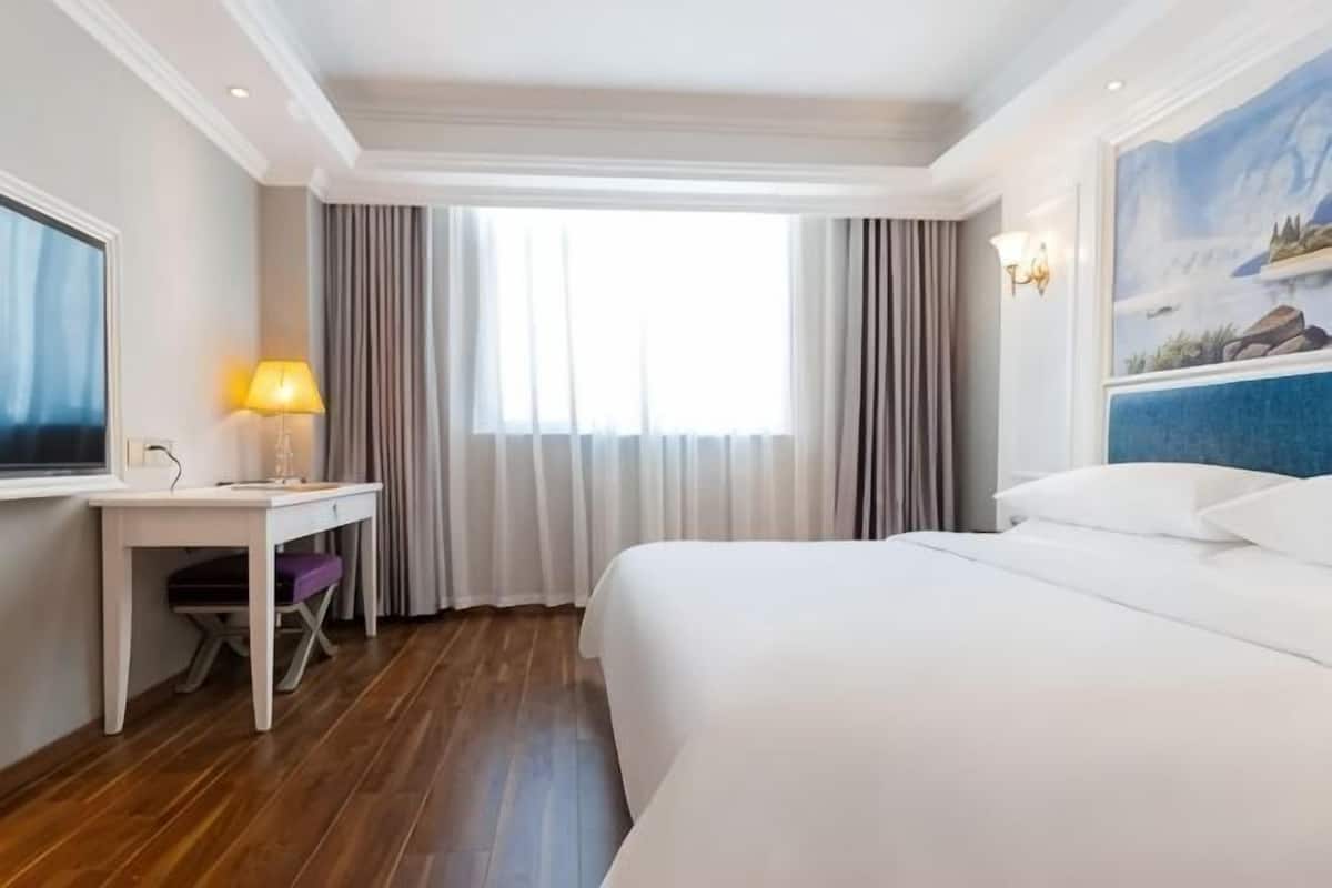 A hotel room with a bed, a desk, a chair, a TV, and a painting on the wall.