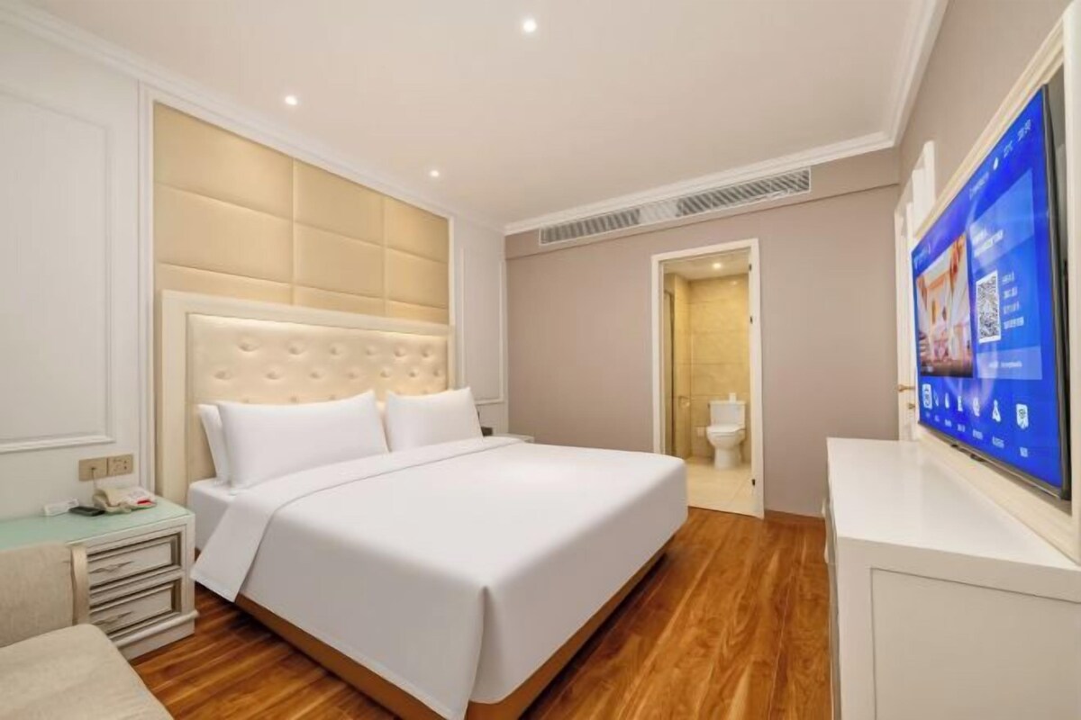 A hotel room with a large bed, a television, and a bedside table.